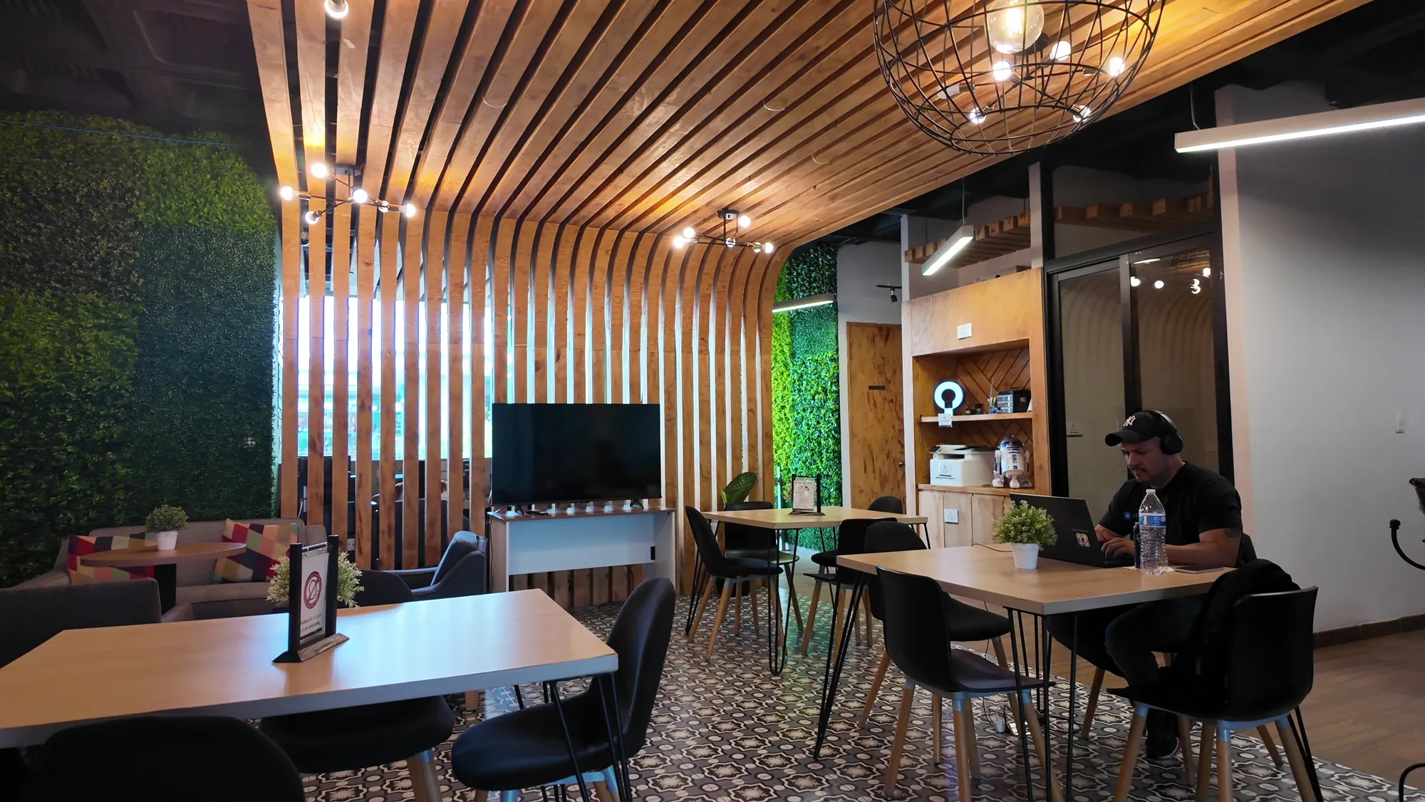 Área de coworking abierta con techo de madera y persona trabajando en laptop